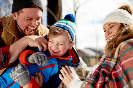 Mother and father enjoying playing in fresh snow during wintertime and tickling their son while...