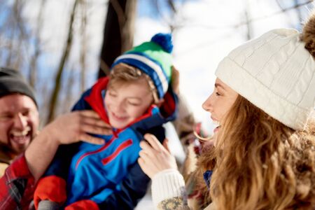 Mother and father enjoying playing in fresh snow during wintertime and tickling their son while laughingの写真素材