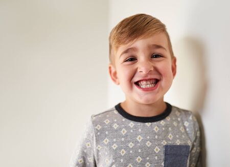Isolated closeup shot of funny, cheerful little kid boy face looking at camera with adorable smile showing teeth, wearing hipster shirt with white backgroundの写真素材