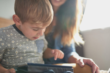 Cute playful kids with loving parents sitting together as a happy family using tablet in bed of...