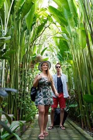 Young happy hipster couple holding hands in tropical plant passaの写真素材