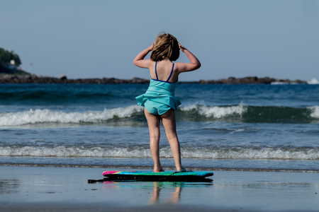 A little girl in blue swimming  suit is surfing at the beachの写真素材