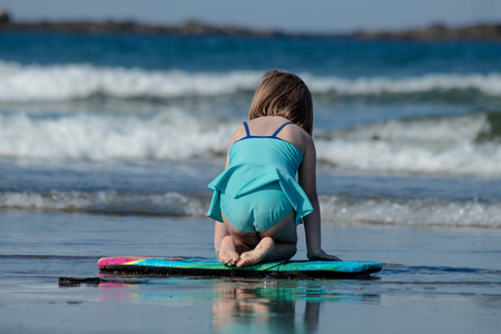 A little girl in blue swimming  suit is surfing at the beachの写真素材