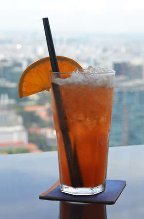 A tall transparent glass with an orange cocktail on the tableの写真素材