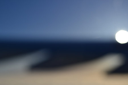 Blurred silhouette of an airplane wing against a blue sky and a bright flare from the sun,...