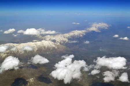 Mountain peaks covered in snow, under the clouds, from the height of the aircraftの写真素材