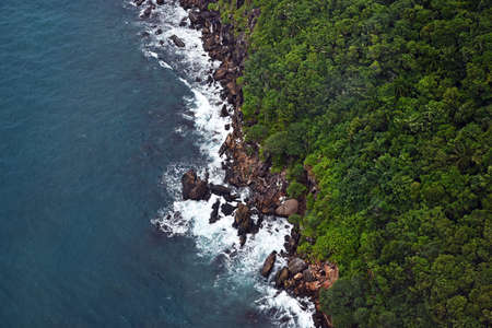 Sea and coastline of the island with rocks and forest, top view, white sea foam.の写真素材