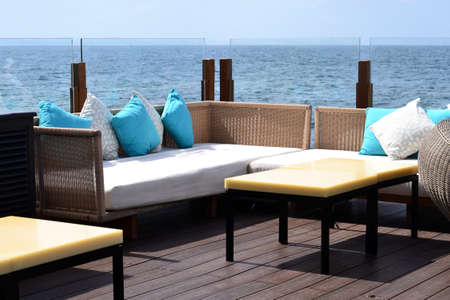 Wicker sofas with soft pillows and low tables in the open air by the sea, and a glass partitionの写真素材