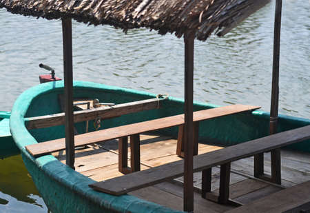 Green painted boat with wooden seats and dry palm canopyの写真素材