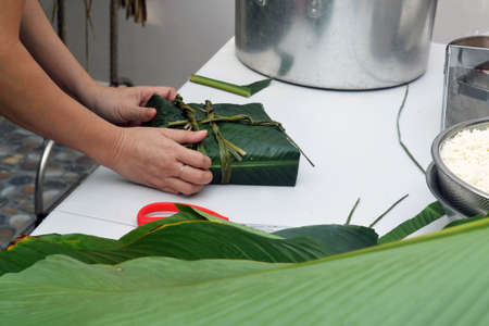 Woman wraps Vietnamese New Year Banh Chung cake into banana leaves and tying it with grass stalksの写真素材