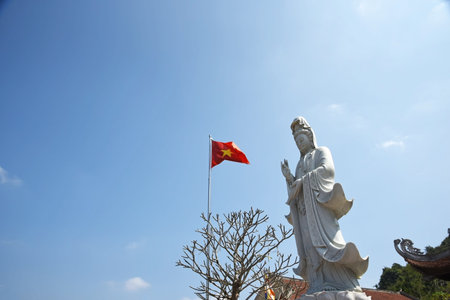 Standing Buddha statue and Vietnam flag against blue skyの写真素材