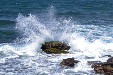 Splashing wave crashes against a large rockの写真素材