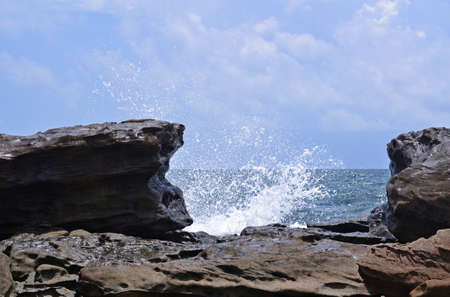 View from the rocky coast to the sea, splashes from the waves, large stones in the foregroundの写真素材