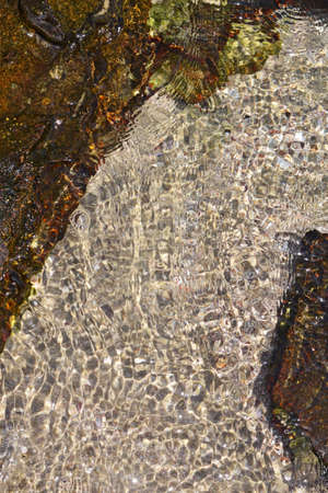 Sand and stones on under a layer of water on a sunny day with beautiful highlightsの写真素材