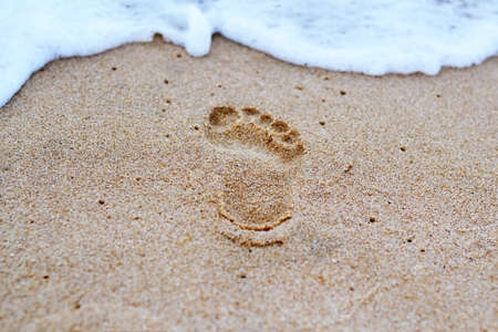 Human footprints in the sand by the sea and sea foamの写真素材