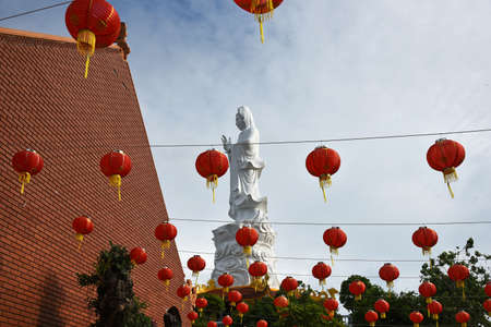 A Buddha statue in a Vietnamese temple against the sky, with red Chinese festive lanterns hanging in the foregroundの写真素材