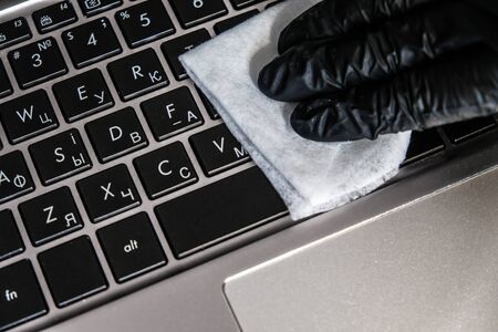Cleaning the laptop keyboard with antibacterial wet wipes. Black glove and white napkin on a black computer. Removing dust and killing bacteria with hand sanitizer. Personal protection in quarantine.の写真素材