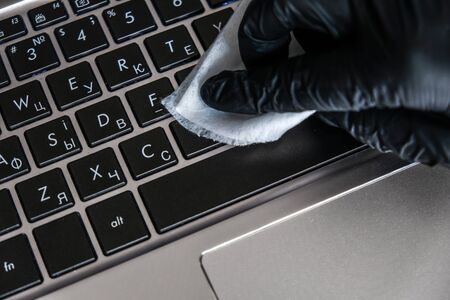 Cleaning the laptop keyboard with antibacterial wet wipes. Black glove and white napkin on a black computer. Removing dust and killing bacteria with hand sanitizer. Personal protection in quarantine.の写真素材