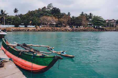 Colorful painted red and green fishing boat tied to the shore. Scenic landscape view from a pier. Local handicraft in Sri Lanka. Blue water. in the sea. Weekend escape from reality to this paradise.の写真素材