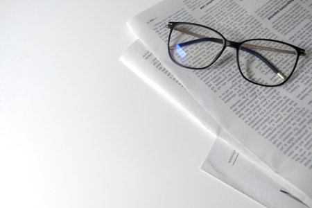 Reading newspaper in isolation. Learning place for homeschooling or workplace for a freelancer. Newspaper and eyeglasses on a white desk with empty space. Education at home. Typical business morning.の写真素材