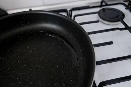 Oily dirty black frying pan left on a gas stove. Unwashed messy cookware after cooking. Unhealthy food choices and lifestyle that leads to obesity. Greasy surface from fried fatty meal in the kitchen.の写真素材