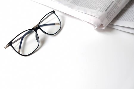 Morning reading at a home office workspace in isolation. Learning place for homeschooling or workplace for a freelancer. Newspaper and eyeglasses on a white desk with empty space. Education at home.の写真素材