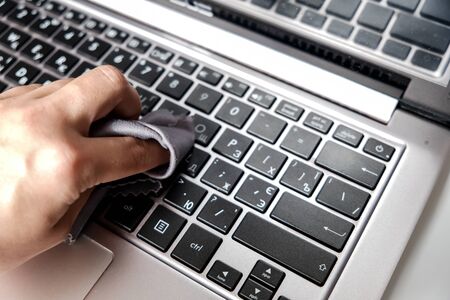 Cleaning the laptop keyboard with a napkin. Closeup white hand on computer. Removing dust and killing bacteria to stay safe at home. Personal protection from corona. Isolation measures in quarantine.の写真素材