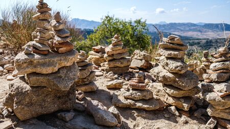 Stacked stones close up from Ronda, Spain. Spiritual piles of rocks (cairn) for calmness and meditation. Mountains in the background at a touristic viewpoint near a famous bridge.の写真素材