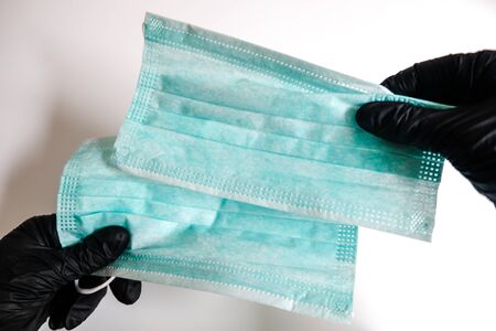 Two hands in black gloves holding a pair of face masks on a white background. Virus spreading and bacteria prevention. Safety measures for self protection in isolation during epidemic. Staying safe.の写真素材
