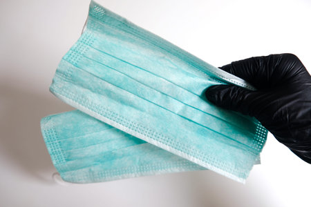 Hand in black glove holding a pair of face masks. Healthy measures to prevent virus spreading. Take...