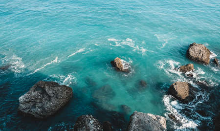 Beautiful blue sea in Nerja, Spain. Waves breaking against the rocks. Powerful stormy nature on a good day with sunny weather. Foam between stones in the water. Close up landscape view.の写真素材