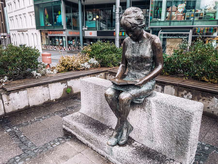 Aachen / Germany - January 2018: Bronze statue of a young girl reading a book called Die Lesende in Aachen city centre. Symbolizes learning process and education importance. Shopping street behind.のeditorial素材