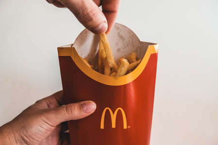 Lviv / Ukraine - April 2020: Close up view of hungry man's hand taking a piece of french fries from Mcdonalds bag. Ordering unhealthy takeaway food from home during coronavirus outbreak isolation.のeditorial素材