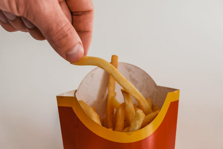 Lviv / Ukraine - April 2020: Close up view of hungry man's hand taking a piece of french fries from...