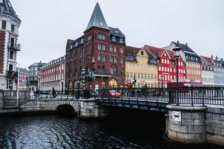 Copenhagen / Denmark - November 2019: Typical forecast day at Nyhavn harbor in Copenhagen. People walking, cars and bicycles moving around. Colorful buildings behind the bridge and grey sky.のeditorial素材