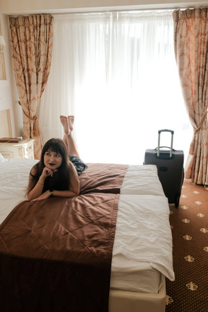 Happy young woman with baggage arrived in a hotel room. First day of summer vacation. Chilling lying...