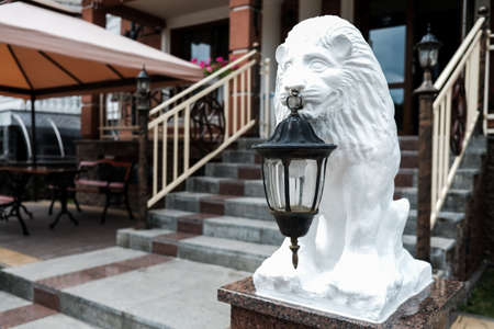 White lion statue holding an old lantern in front of a hotel or restaurant facade. Stairs in the background. Hospitality concept. Sightseeing in eastern Ukraine. Lviv, historical old city of lions.の写真素材