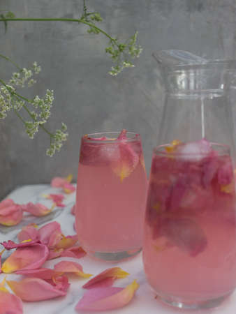 Summer pink cocktail with rose petals and ice cubes on a gray backgroundの写真素材