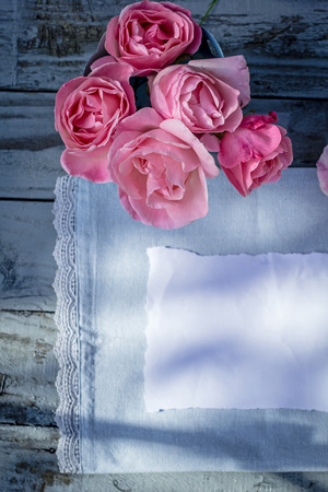 Beautiful, pink roses on wooden, rustic background with white paper and copy spaceの写真素材