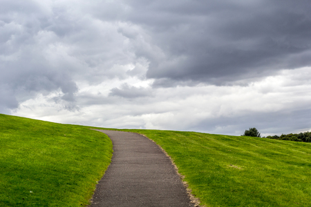 Natural background with a path up the hill, green grass and clouded skyの写真素材