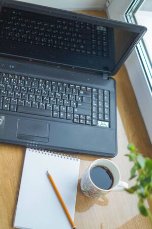 Laptop (notebook) with cup of coffee and notepad with pen remote work on the windowsillの写真素材