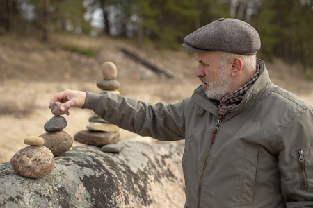 Elderly man holding round stones in his hands, stone balancingの写真素材