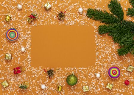 on a bright orange background multicolored Christmas toys, green tree branch, snow, top view, copy space in the centerの写真素材