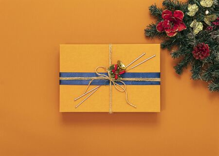 on a bright orange background multicolored Christmas toys, branch green tree, orange box gift with a blue ribbon, top view, copy space in the centerの写真素材