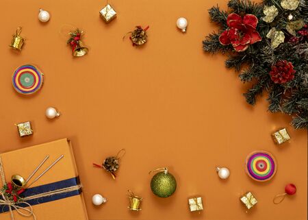 on a bright orange background multicolored Christmas toys, branch green tree, orange box gift with a blue ribbon, top view, copy space in the centerの写真素材