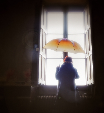 A MELANCHOLIC WOMAN TO THE WINDOW WITH AN ORANGE UMBRELLAの写真素材