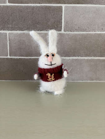 Hand made cute clever knitted rabbit toy or hare in red sweater with horse and book on brick wall background standing on the table. Photoの写真素材