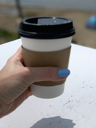 Woman Hand with manicure holding paper cup of coffee on natural morning background. Sea background.の写真素材