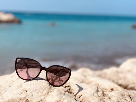 Sunglasses on the stone beach on sea backgroundの写真素材