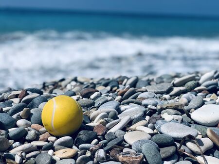 yellow tennis ball on the pebbles beach on sea backgroundの写真素材